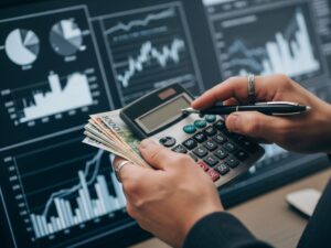 Hands holding money with a calculator and financial graphs in the background, representing personal budgeting.